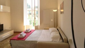 Une chambre d’hôtel avec un lit, un bureau, une chaise, une télévision, une fenêtre et une lampe.