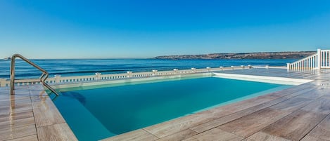 Una piscina al aire libre, sombrillas, sillones reclinables de piscina