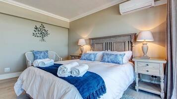 A neatly made bed with white and blue bedding, two bedside tables with lamps, a wall-mounted air conditioner, and a decorative wall piece.