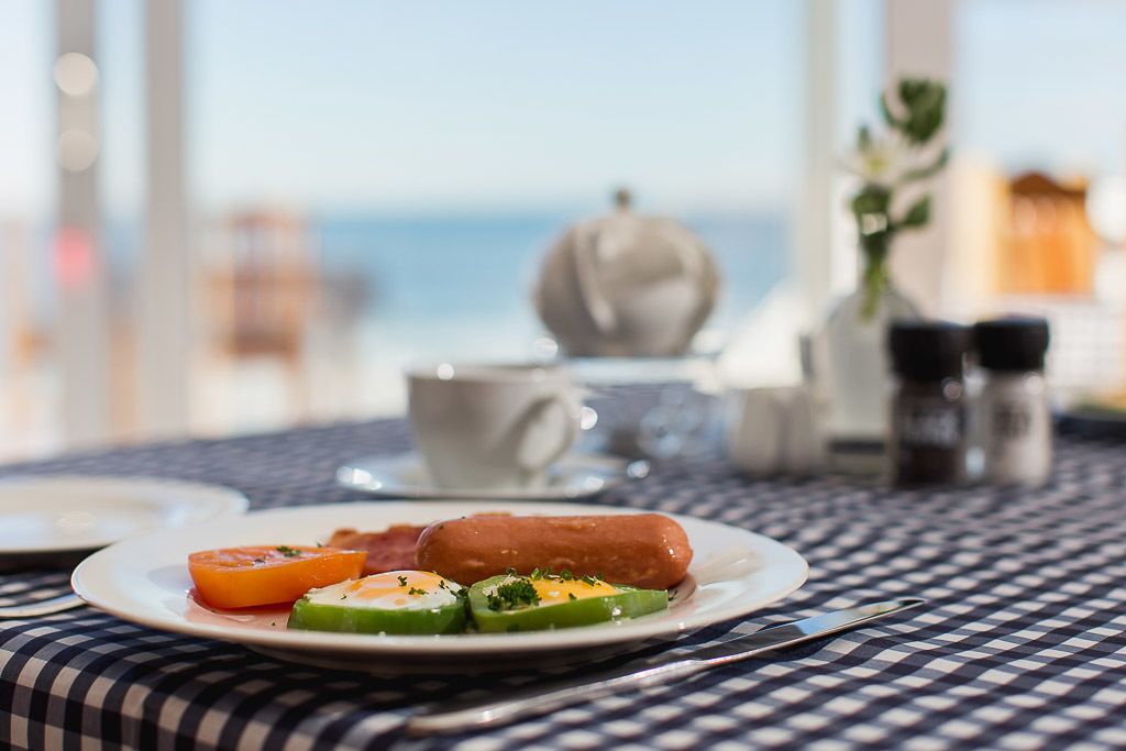 Mesa de café da manhã com um prato de comida, uma xícara e um saleiro sobre uma toalha quadriculada.