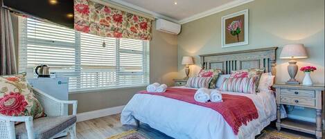 A bedroom with a bed, bedside tables, a chair, a window with blinds, and a wall-mounted air conditioner.