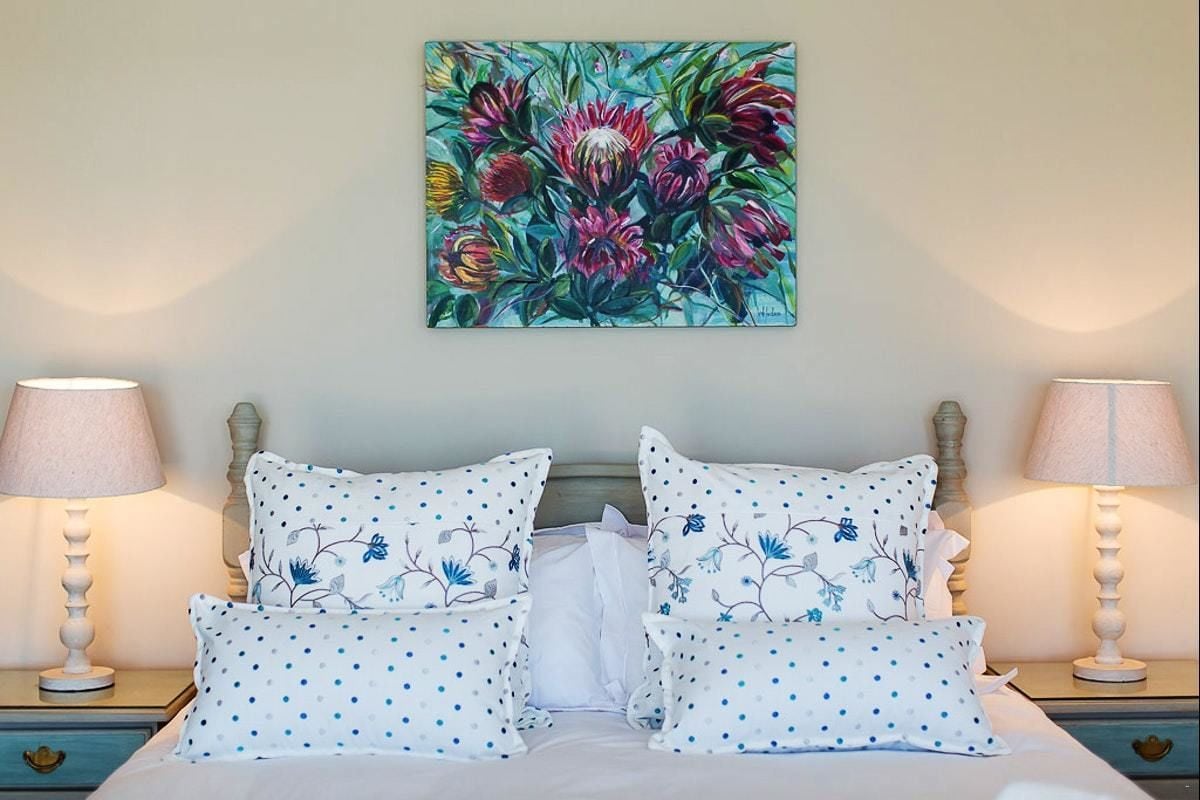 A bedroom with a bed, two bedside tables, two lamps, and a floral painting on the wall.