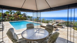 Un espacio al aire libre techado con piscina, asientos y vista al océano.