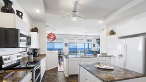 Una cocina moderna con una isla grande, electrodomésticos de acero inoxidable y vistas al océano.