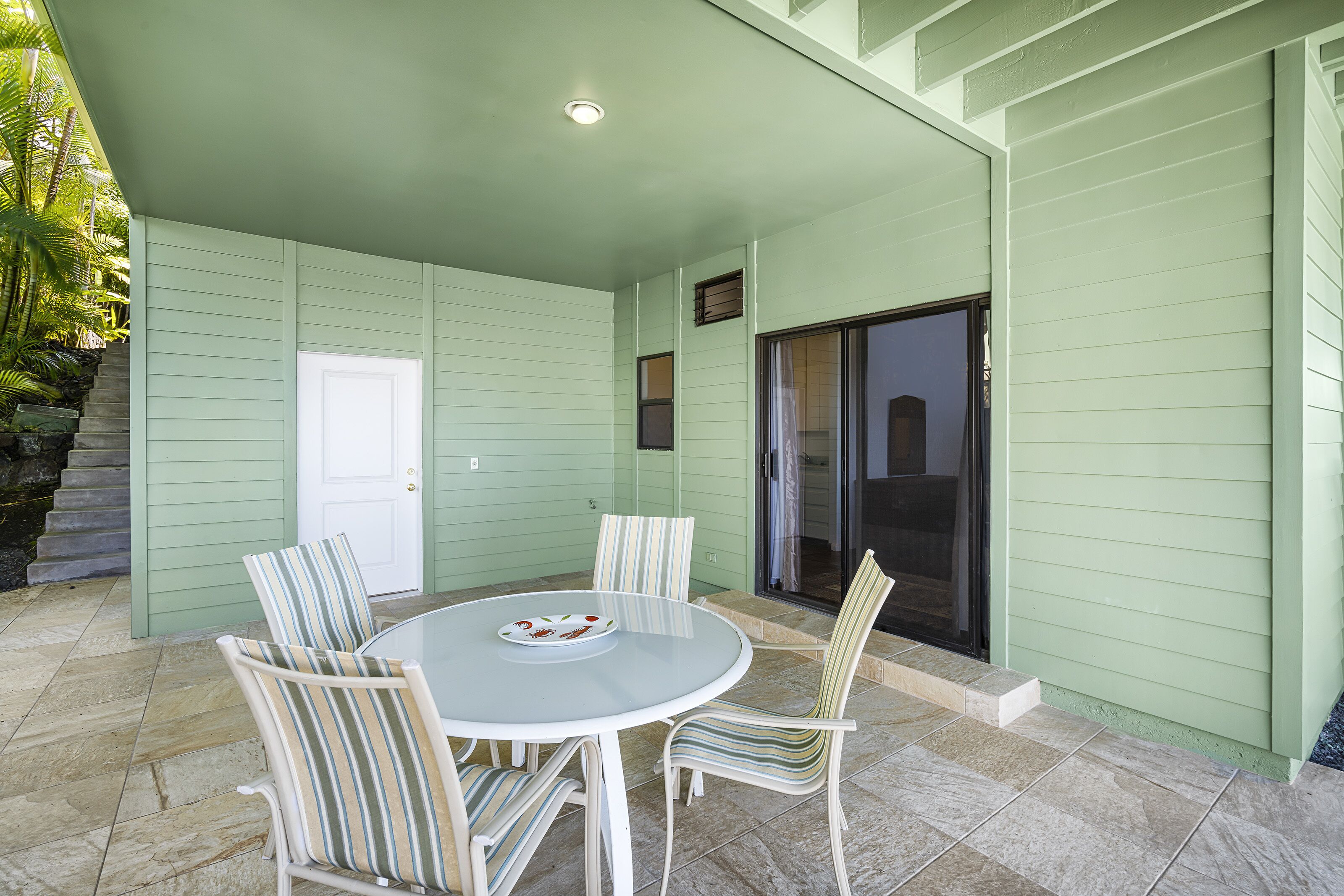 A covered patio with a round table and striped chairs, a white door, and a sliding glass door.