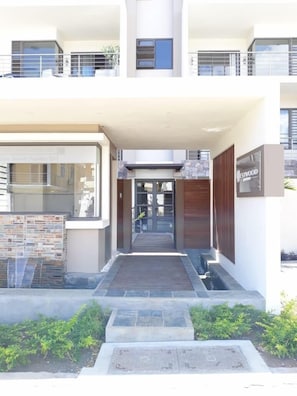 Stylish entrance with a welcoming pathway and garden area, leading to a modern building with large windows.