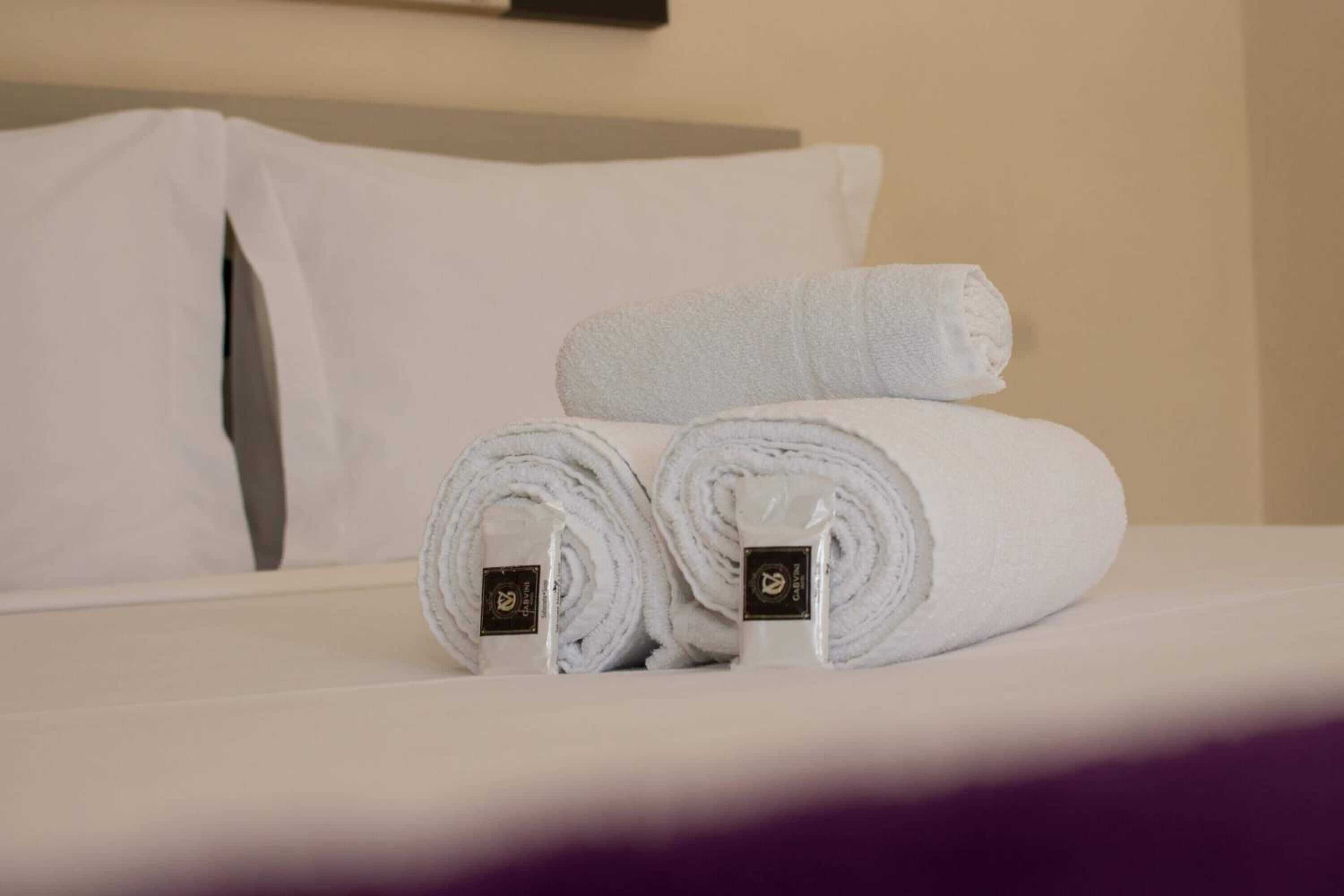 A neatly made bed with white linens, including rolled towels and a pillow.