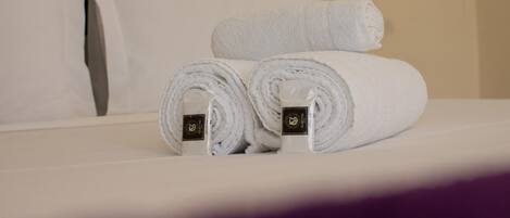 A neatly made bed with white linens, including rolled towels and a pillow.