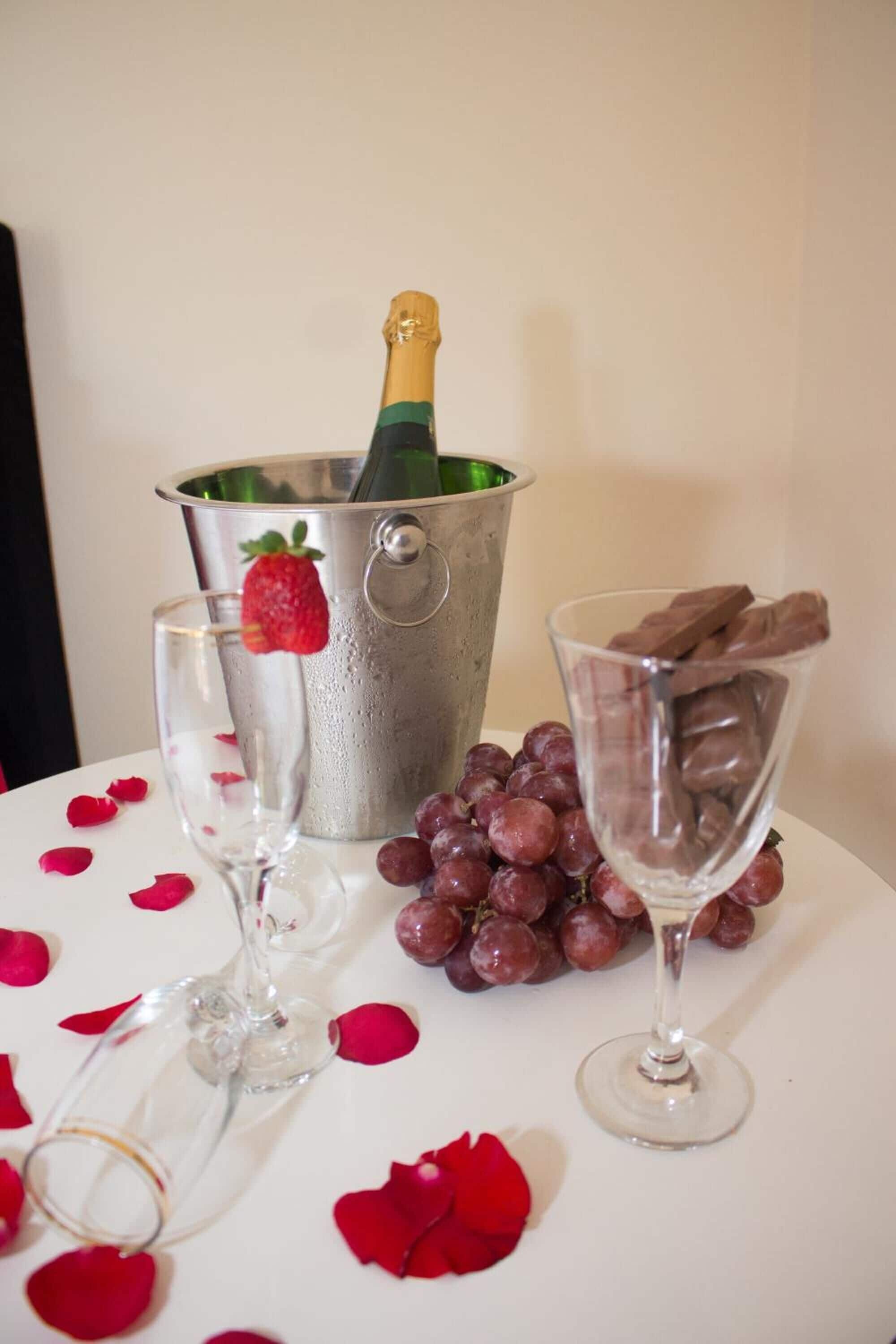 Een tafel met een champagnefles, een glas, een schaal druiven en een glas chocolademelk.