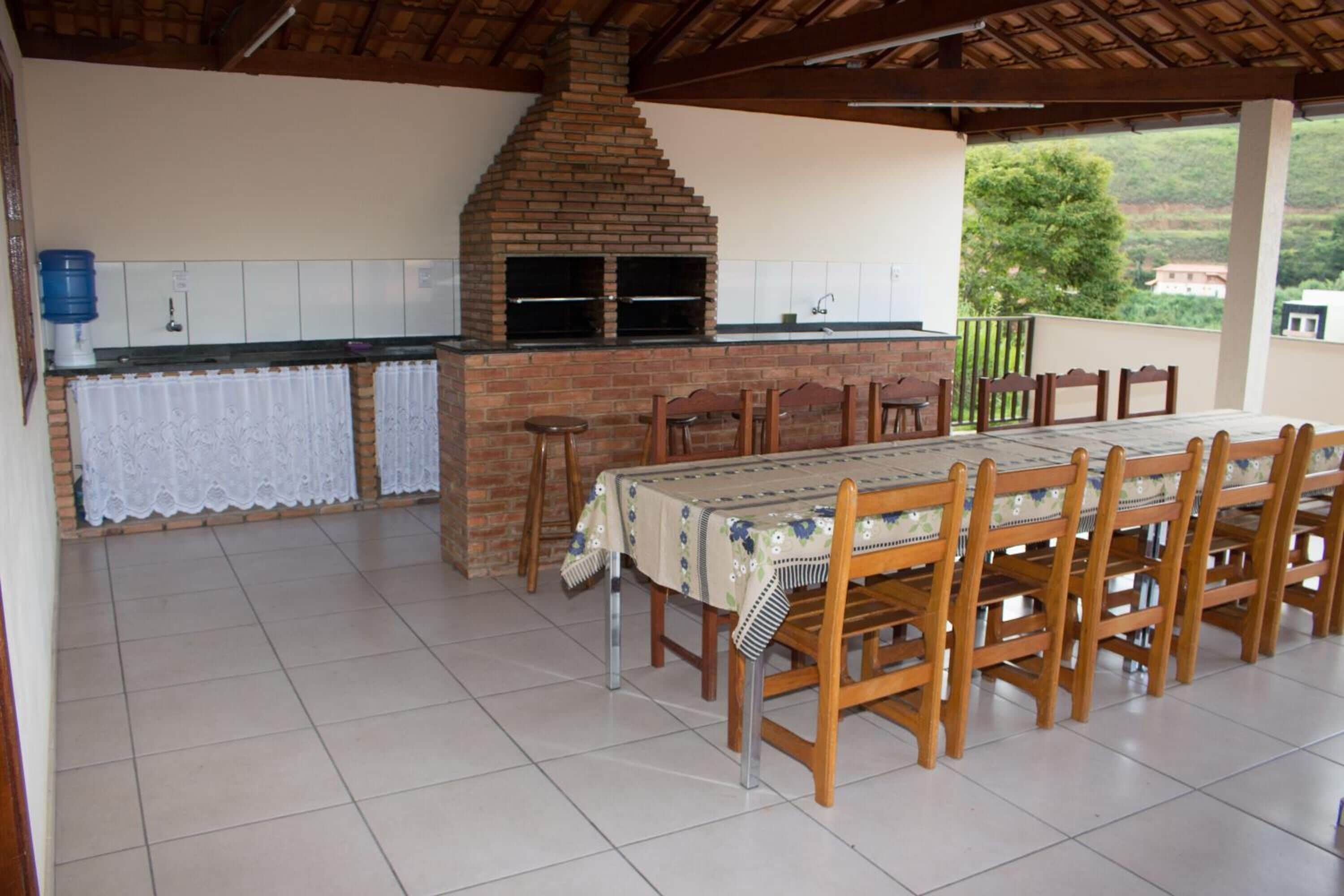 Una cocina exterior con horno de ladrillo, una mesa de comedor con sillas y un dispensador de agua.