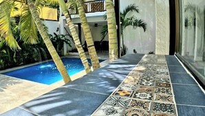 Ein moderner Poolbereich mit Fliesenboden, Palmen und einer Glasdoor, die zu einer überdachten Terrasse führt.