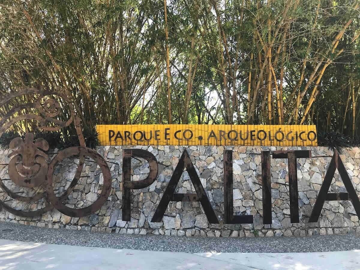 En skylt med texten ”PARQUE E CO. ARQUEOLÓGICO” och ”OPALITA”, med en stenmur och en metallskulptur i bakgrunden.