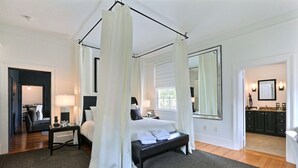 A bedroom with a four-poster bed, a large mirror, and a view of the bathroom.