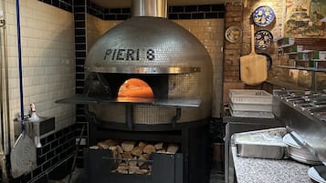 Een keuken met een houtgestookte oven, betegelde muren en een mozaïekvloer.
