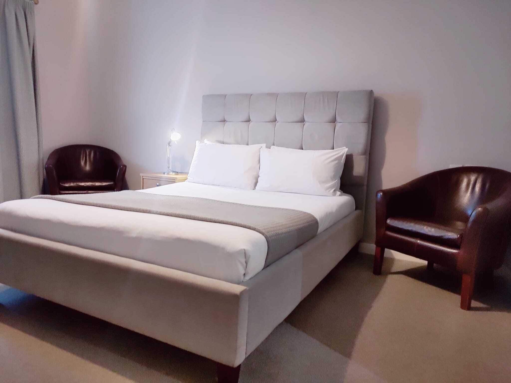 A neatly made bed with a tufted headboard, two bedside tables with lamps, and two leather chairs.