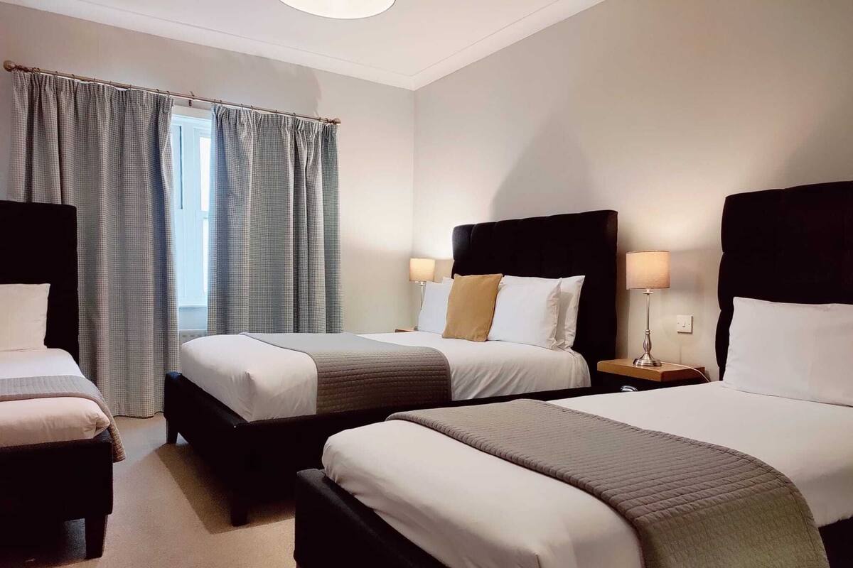 A hotel room with two beds, a window with curtains, and a nightstand with a lamp.