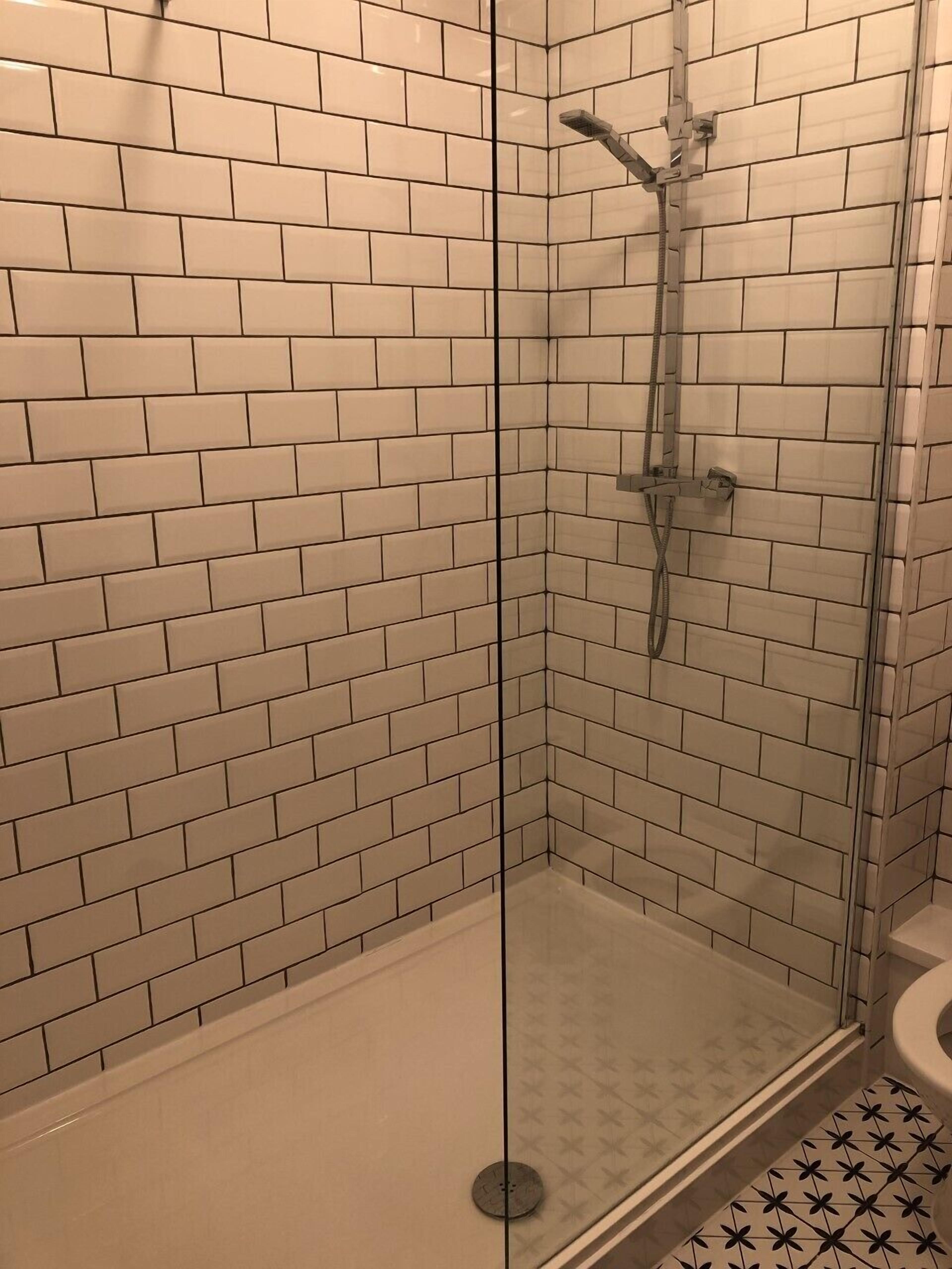A glass-enclosed shower with white subway tiles on the walls and floor.