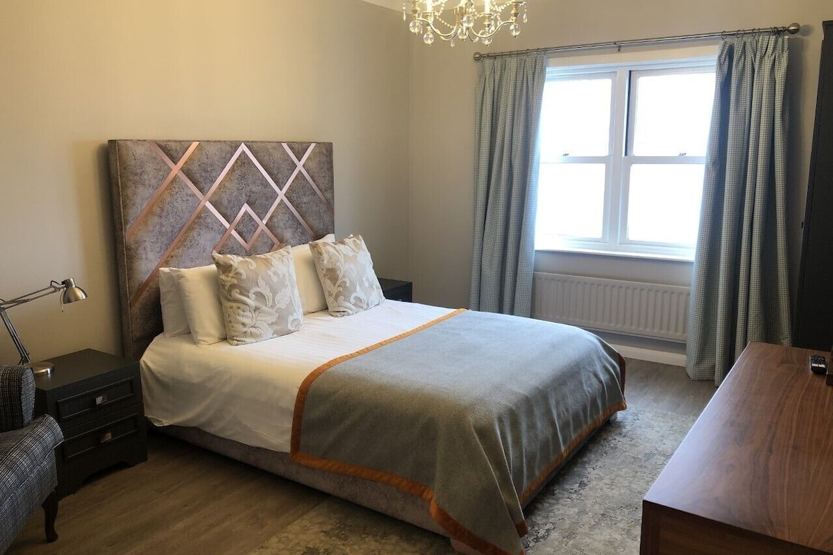 A bedroom with a bed, a nightstand, a desk, and a window with curtains.