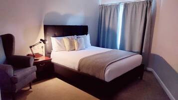 Een netjes ingerichte hotelkamer met een bed, een stoel, een nachtkastje en een lamp.