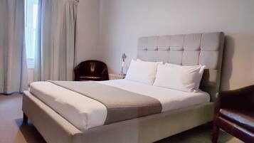 A neatly made bed with a headboard, a bedside table with a lamp, and a chair.