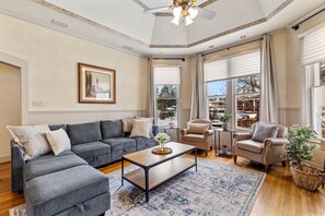 Un salon spacieux avec un canapé d’angle gris, une table basse en bois et un fauteuil beige.