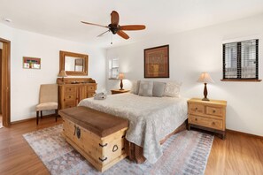 A bedroom with a bed, a wooden chest, a desk, a chair, a mirror, a ceiling fan, and a window with blinds. - Skyline Stargazing Cabin with hot tub (Flagstaff)