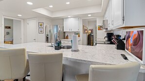 Una cocina moderna con armarios blancos, encimera de mármol y una isla grande con asientos.