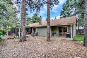 A single-story house with a covered patio, a chimney, and a small backyard with trees and a gravel area. - Skyline Stargazing Cabin with hot tub (Flagstaff)