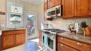 A kitchen with wooden cabinets, a stainless steel stove, a microwave, and a window with a view of the outside. - Heated Pool Access | 5*Clean | Flex Cancelation (Savannah)