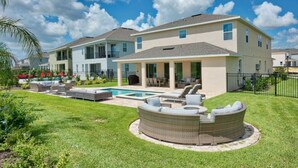 A two-story house with a covered patio area, a swimming pool, and a circular outdoor seating area.