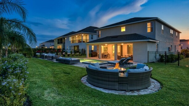 A modern two-story house with a covered patio, a swimming pool, and a circular outdoor seating area with a fire pit.
