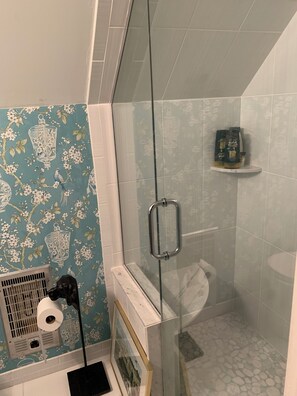 Een badkamer met een douchecabine van glas, een toilet en een plank met toiletartikelen.