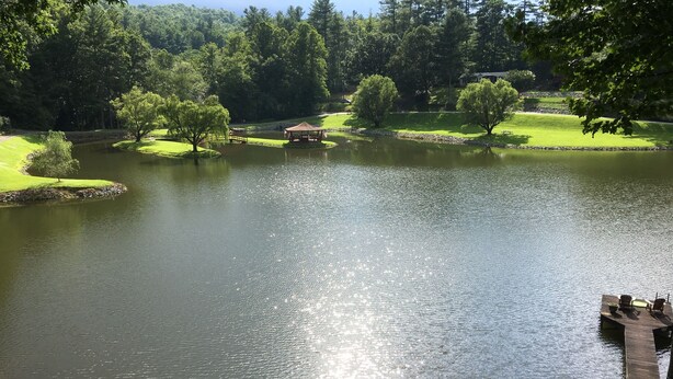 A tranquil lake with a wooden dock and a gazebo in a lush, green park setting.