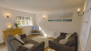 Ett vardagsrum med två soffor, ett träskåp, en tv och ett fönster med utsikt över havet.