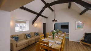 Un coin repas avec une table en bois dressée pour six personnes, un canapé et une fenêtre avec des rideaux.