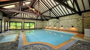 Une piscine intérieure dotée d’un sol carrelé, d’un mur en briques et d’une structure de plafond en bois.