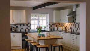 Une cuisine moderne avec des meubles blancs, un crédence à carreaux noirs et blancs, un îlot central en bois avec des tabourets et une fenêtre qui laisse entrer la lumière naturelle.