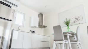 A modern kitchen with white cabinetry, a stainless steel range hood, and a dining area with a glass table and two chairs. - The Palm Leaf Apartments (Noord)