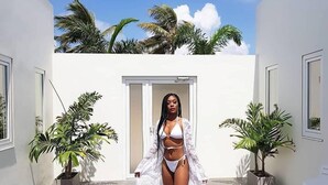 A woman in a white bikini and cover-up standing in a courtyard with potted plants and a door in the background. - The Palm Leaf Apartments (Noord)