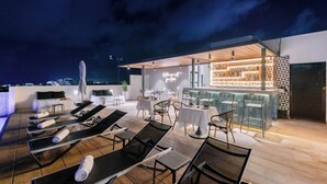 Une terrasse sur le toit équipée de chaises longues, d’un bar et d’un espace détente avec des tables et des chaises.