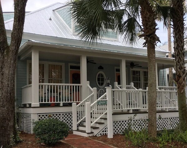 A two-story house with a covered porch, white railings, and a small garden area.