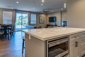 A modern kitchen with a large island, built-in oven, and a dining area with a table and chairs. - Grill Deck + Game Lounge | Mins to Downtown Paso | Westside Riley House (Paso Robles)