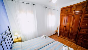 A bedroom with a bed, curtains, a wooden wardrobe, and a nightstand with a lamp. - San Antonio Rural House. Villa 3 (3 bedrooms) (Cabra (Córdoba))