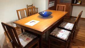 Une table de salle à manger en bois, sur laquelle se trouve un saladier bleu, six chaises avec des coussins à motifs et un set de table blanc avec un stylo.
