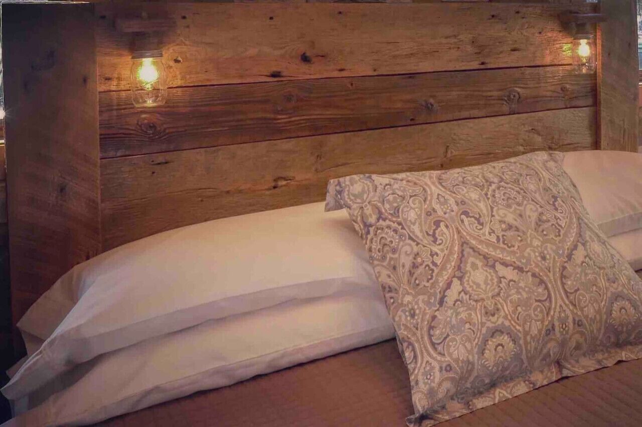 Cabecera de madera con una lámpara, una cama con ropa de cama blanca y un cojín decorativo estampado.