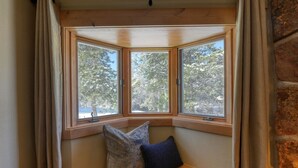 A bay window with two cushions, a wooden bench, and a view of trees.