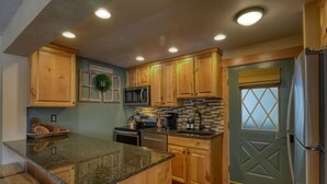 A kitchen with wooden cabinets, granite countertops, a built-in microwave, and a refrigerator.