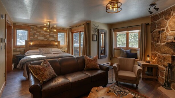 A cozy room with a bed, leather sofa, and a stone fireplace.