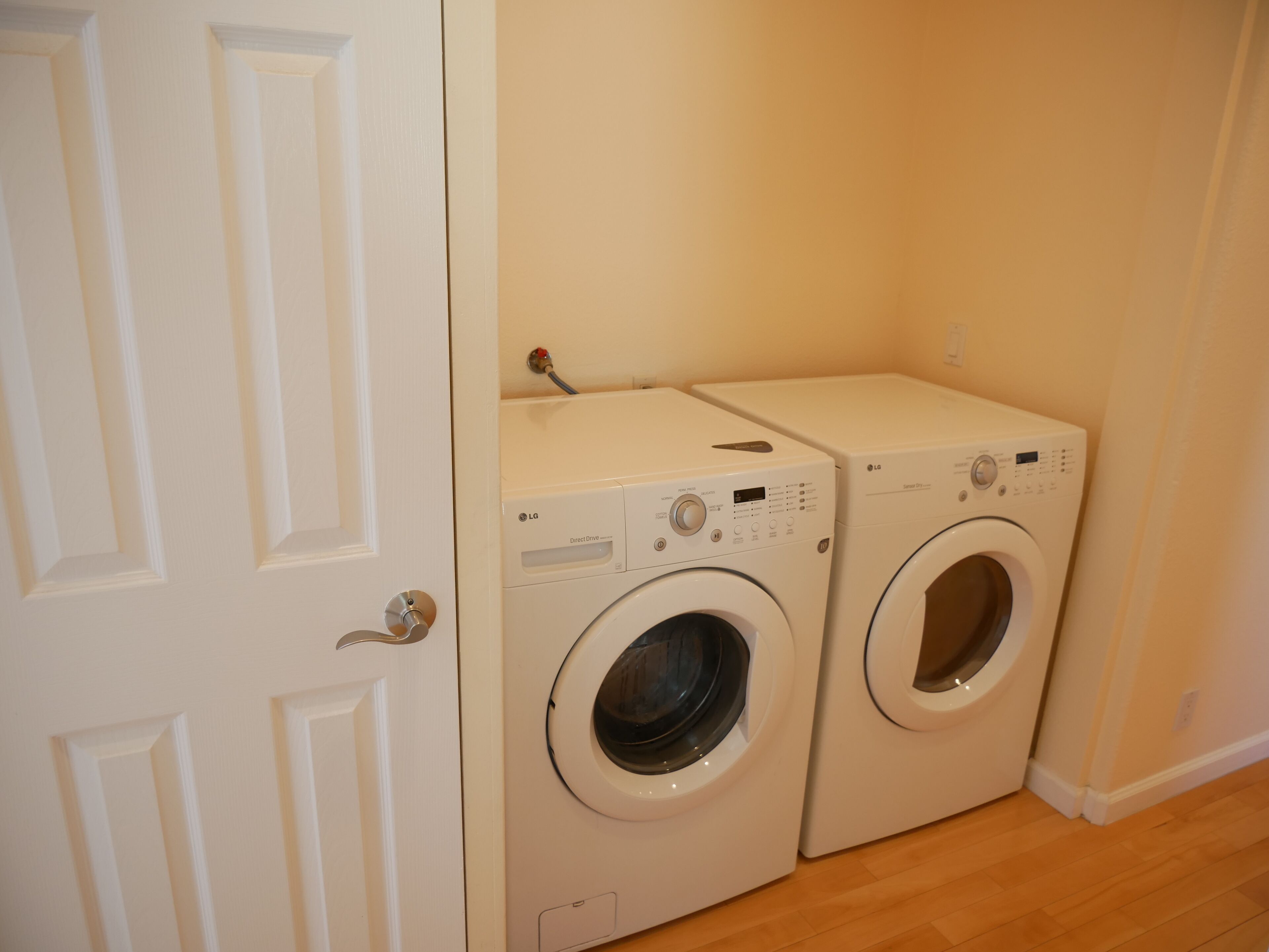 A laundry room with two white front-loading washing machines and a white door.