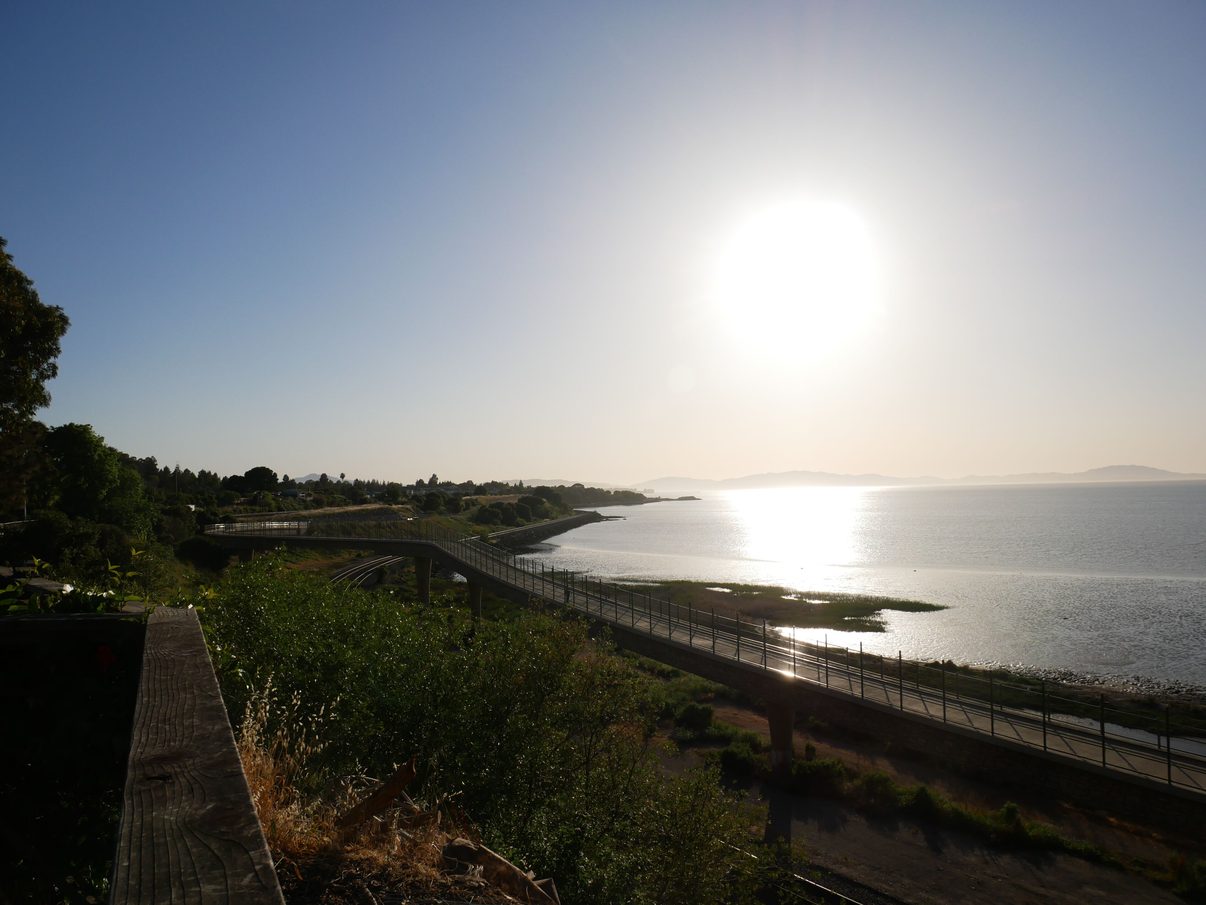 A coastal bridge with a clear view of the sea and distant mountains.
